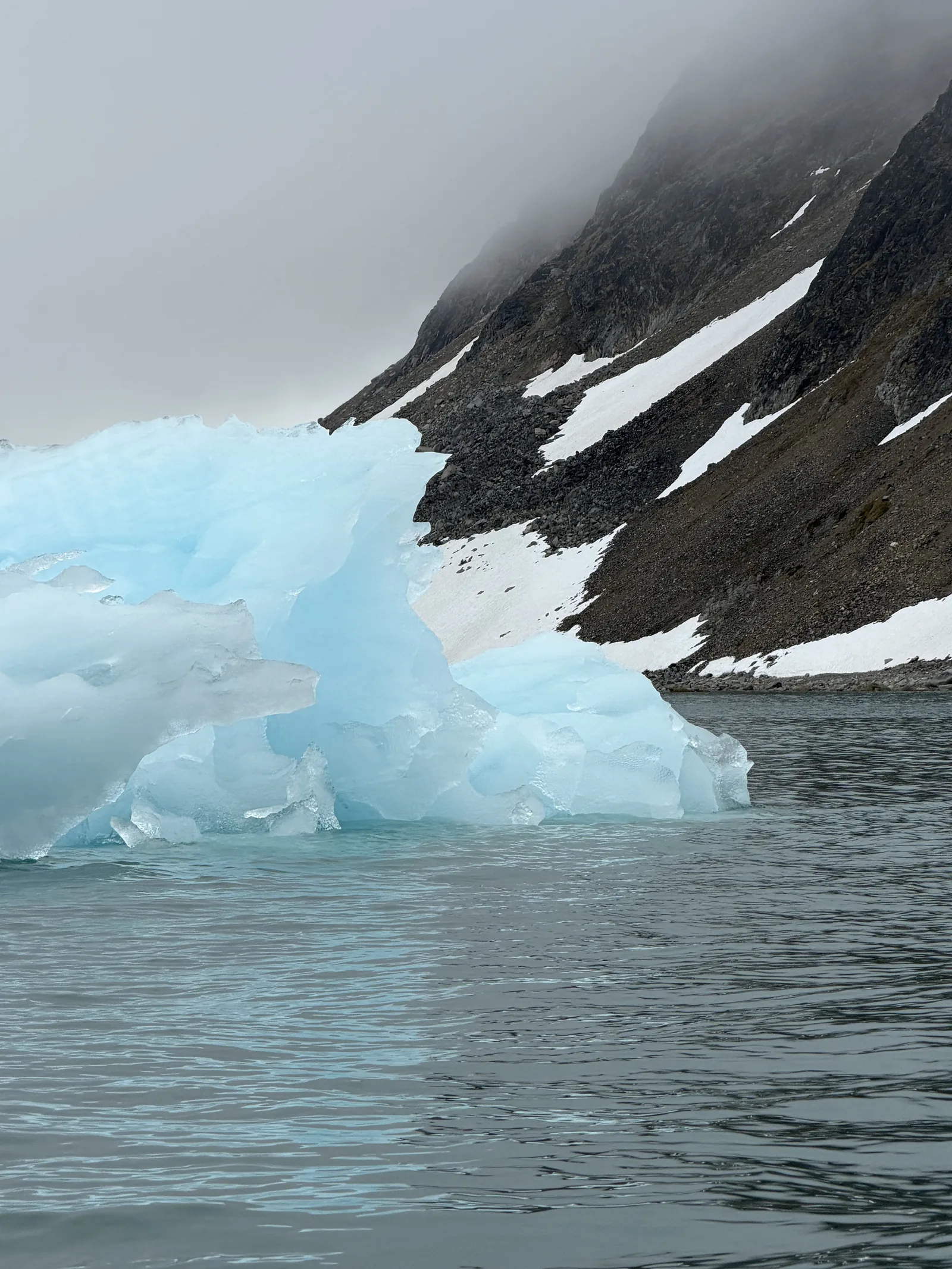 A vivid blue iceberg below a dark mountain